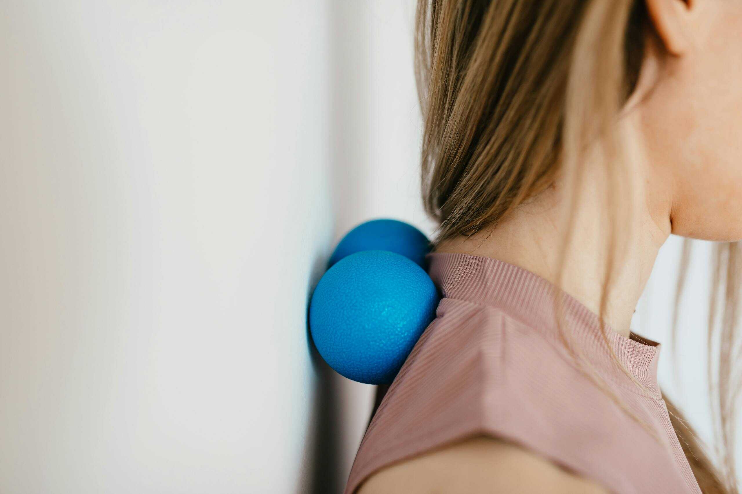 Close-up of woman using blue massage balls for neck relief during her injury rehabilitation.